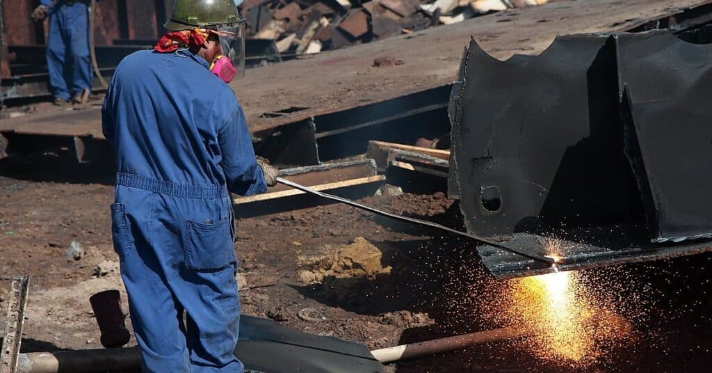 Construction worker welding scrap metal from a ship.